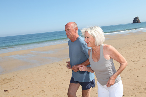 Senior couple jogging on a sandy beach - Foto, Imagen