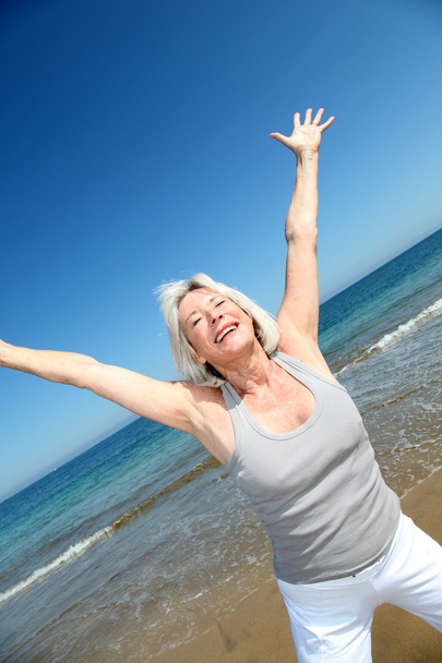 Senior woman doing stretching exercises on the beach - Фото, изображение