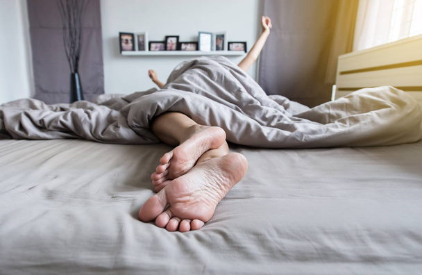 Primer plano de los pies descalzos, y estirar perezosamente en la cama después de despertarse por la mañana
 - Foto, Imagen