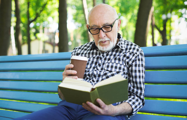 Elderly man in casual reading outdoors - Zdjęcie, obraz