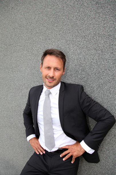 Smiling handsome businessman leaning on concrete wall - Foto, immagini