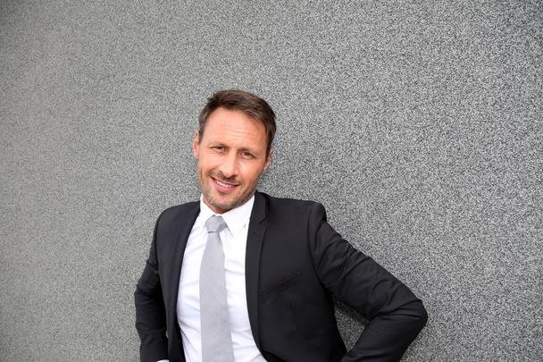 Smiling handsome businessman leaning on concrete wall - Valokuva, kuva