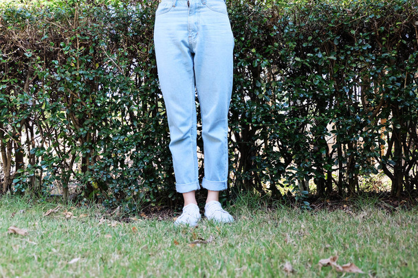 Hipster lässige weiße Turnschuhe. Frau steht mit weißen Schuhen und blauen Jeanshosen auf grünem Gras Natur Hintergrund ideal für jeden Einsatz. - Foto, Bild