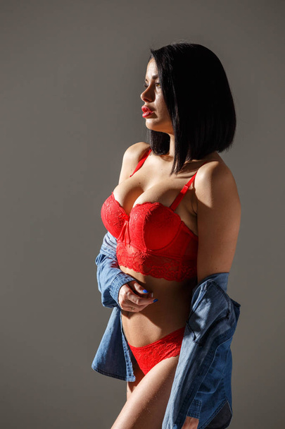 Studioaufnahme der schönen brünetten Frau in sexy roten Dessous. junge Schönheit Frau steht im Seitenlicht auf grauem Studiohintergrund  - Foto, Bild