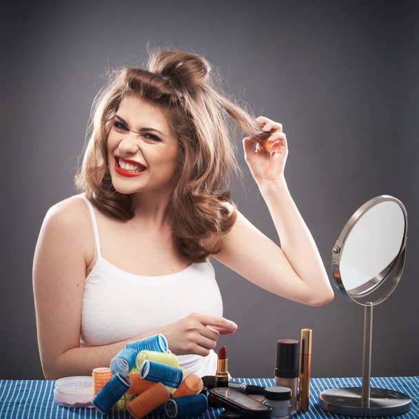 portrait of young woman taking off curlers from hair on gray background, troubles with curly hair and hairstyle concept  - Foto, Imagen