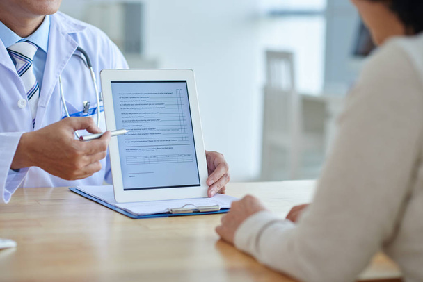 врач указывает ручкой на цифровой планшет, пациентка слушает его
 - Фото, изображение