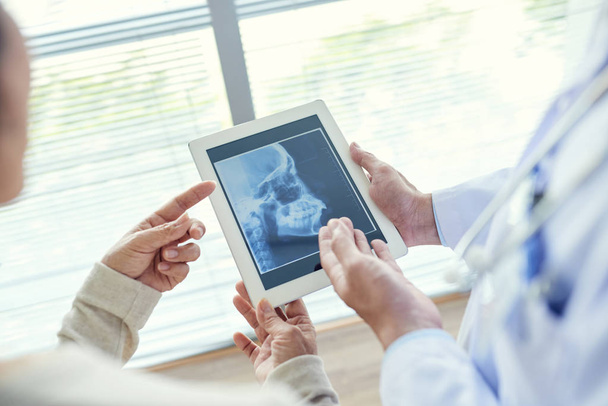 οδοντίατρος δείχνει οδοντιατρική ακτινογραφία σε ασθενή με τη βοήθεια της ψηφιακή ταμπλέτα  - Φωτογραφία, εικόνα