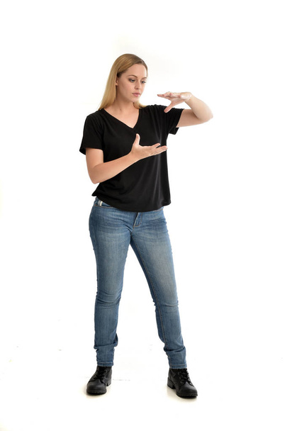 full length portrait of blonde girl wearing basic black shirt and jeans, standing pose on white background. - Photo, Image
