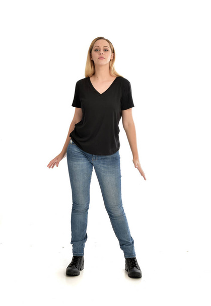 基本的な黒の t シャツとジーンズを身に着けているブロンドの女の子は、白い背景の上の立ちポーズの完全な長さの肖像画. - 写真・画像