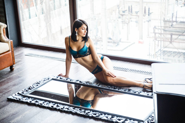 Studio shot of beautiful brunette woman wearing sexy lingerie. Beautiful sporty girl lying on mirrors at apartments interior - 写真・画像