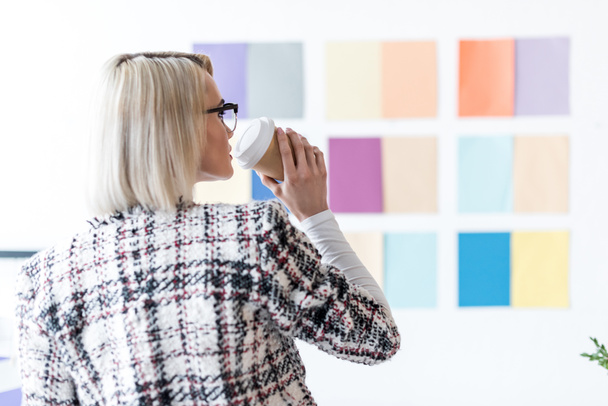editor de revista de moda atraente beber café e olhar para a paleta de cores na parede
 - Foto, Imagem