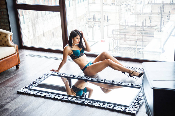 Studio shot of beautiful brunette woman wearing sexy lingerie. Beautiful sporty girl lying on mirrors at apartments interior - Φωτογραφία, εικόνα