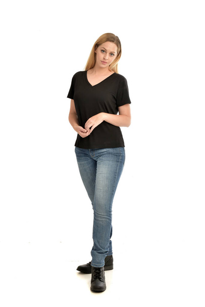 full length portrait of blonde girl wearing basic black shirt and jeans, standing pose on white background. - Photo, Image
