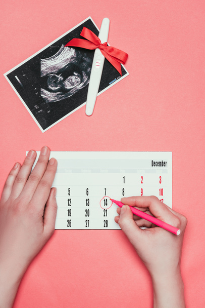 частичное представление женщины, делающей запись в календаре, ультразвуковое сканирование и тест на беременность с лентой, изолированной на розовом
 - Фото, изображение