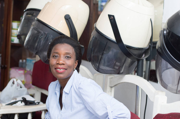 This young woman is sitting next helmets waiting her turn for her hairstyle. - Photo, Image