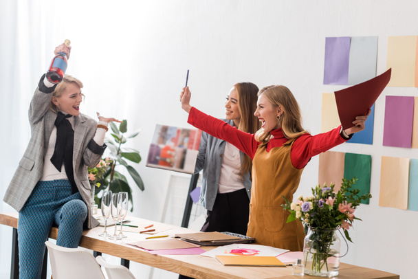 emocionados editores de revistas gritando y celebrando con champán en la oficina moderna
  - Foto, Imagen