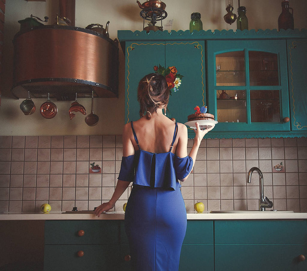 Donna rossa in abito blu che tiene torta di cioccolato compleanno in cucina
 - Foto, immagini