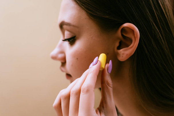 cute young girl puts in ears yellow earplugs against noise - Foto, afbeelding