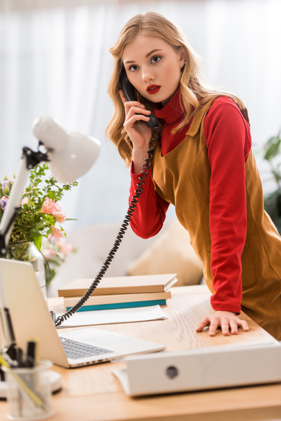 stylish businesswoman talking on phone at workplace with laptop and documents - Foto, imagen