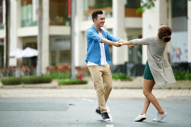 Retrato de pareja joven despreocupada bailando de la mano en la calle y sonriendo, disfrutando de la cita
 - Foto, imagen