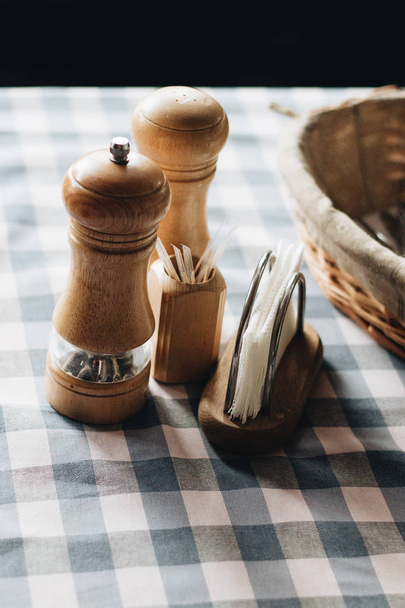 Salz- und Pfeffermühlen aus Holz, Zahnstocher und Ständer mit Papierservietten auf Tischdecke  - Foto, Bild