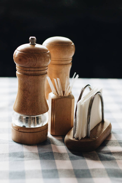 wooden salt and pepper mills, toothpicks and  stand with paper napkins on tablecloth  - Foto, Imagen