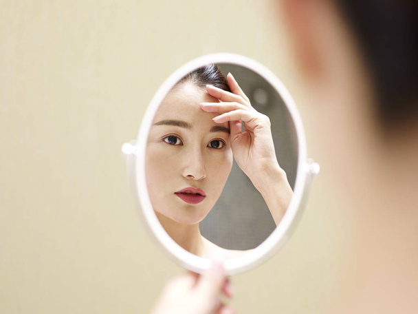 鏡で自分で見ている若いアジア女性 - 写真・画像