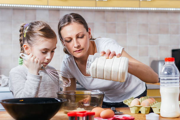 Mother and daughter making dough at home kitchen - Фото, изображение