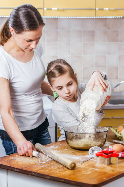 Mother and daughter pouring flour into bowl - Fotó, kép