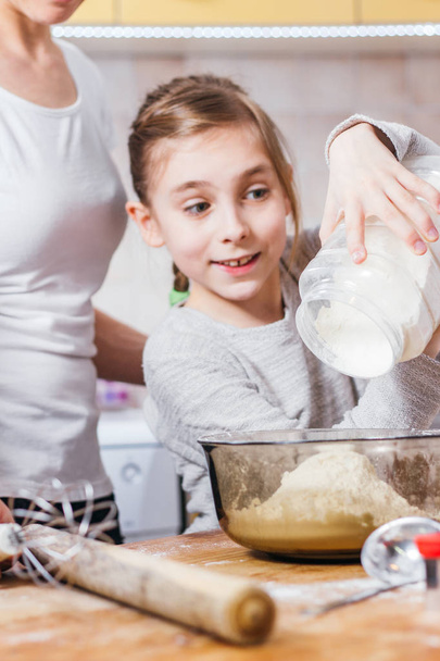 Mother and daughter pouring flour into bowl - Photo, Image