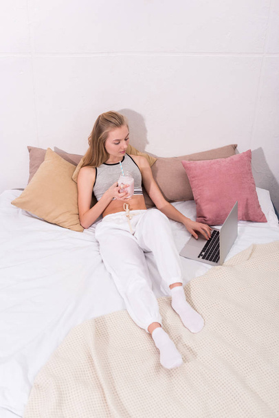 vue grand angle de la jeune femme avec milkshake en pot de maçon de travail avec ordinateur portable au lit
 - Photo, image