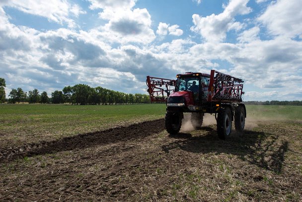 Vista frontal da máquina para aplicação de fertilizantes no campo com árvores e céu azul nublado no fundo
 - Foto, Imagem
