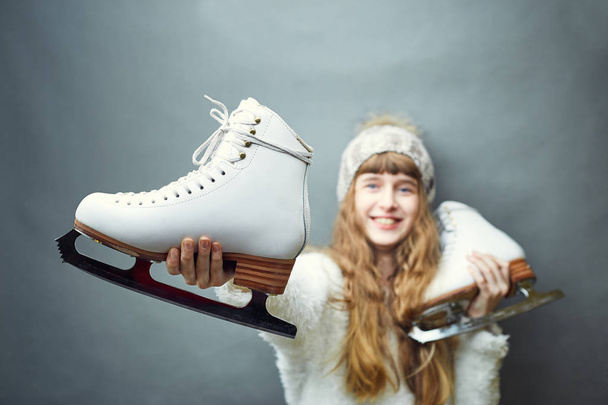 A girl with skates in her hands in a white sweater and hat. - Foto, Imagem
