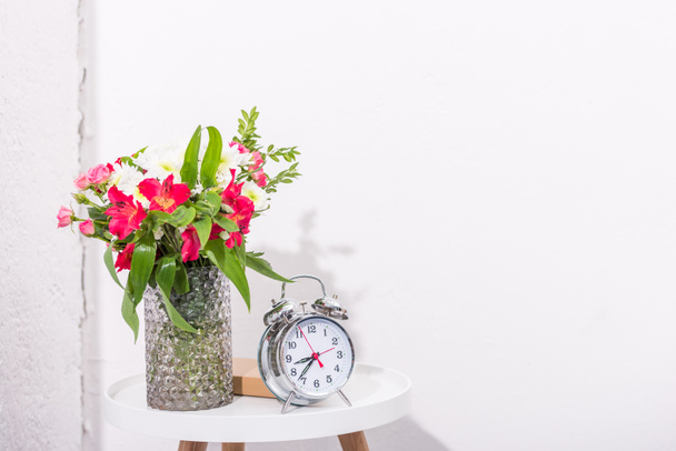 винтажный будильник на столе с цветами в вазе
 - Фото, изображение