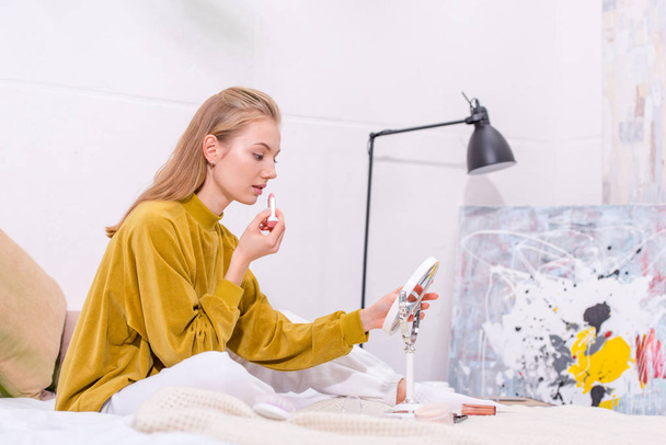 beautiful young woman applying lipstick on bed at home - Fotografie, Obrázek