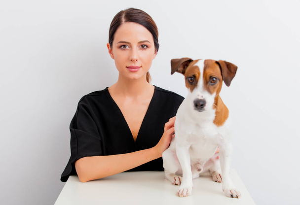 Pretty redhead caucasian woman in black dress with dog sitting at white table in lagom style on white background - Photo, Image