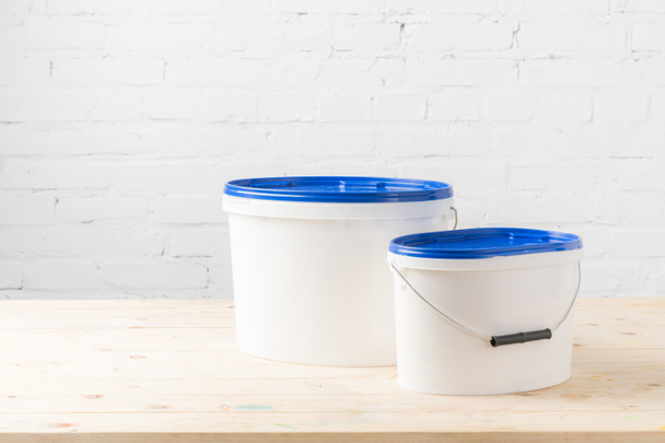 two plastic buckets with paints on wooden table - Foto, afbeelding