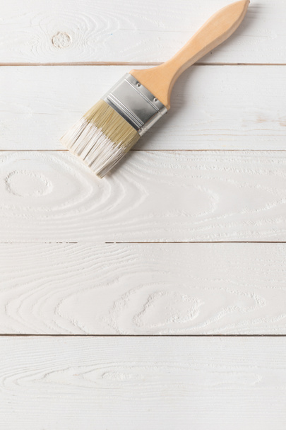 top view of brush in white paint on painted wooden surface - Foto, immagini