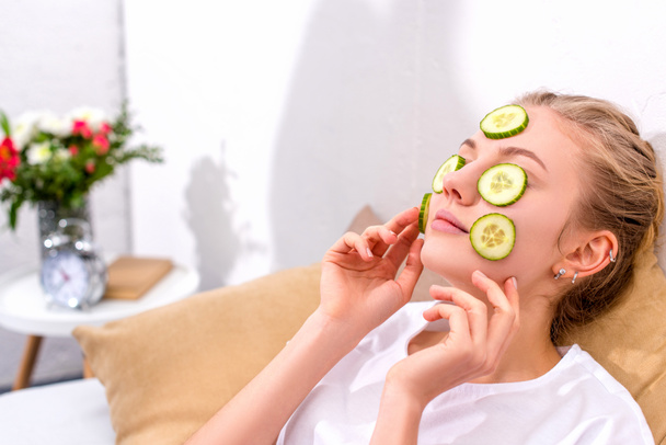 young woman applying cucumber slices on face at home - Fotografie, Obrázek