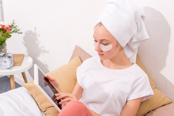 jeune femme avec des patchs faciaux cosmétiques en utilisant une tablette à la maison
 - Photo, image