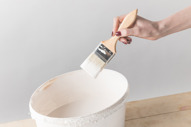 cropped image of woman holding brush in white paint above bucket - Фото, изображение