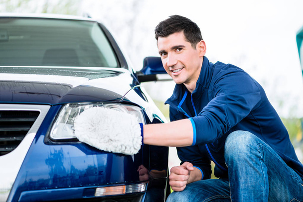 Smiling man cleaning the headlamp on his car - Foto, imagen