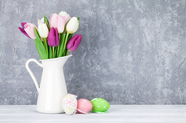 Easter eggs and colorful tulips bouquet in front of stone wall. With copy space - Valokuva, kuva