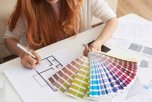 Lähikuva muotokuva nuori nainen työskentelee pohjapiirrokset ja väri swatches valitsemalla sisustus uuden talon
 - Valokuva, kuva
