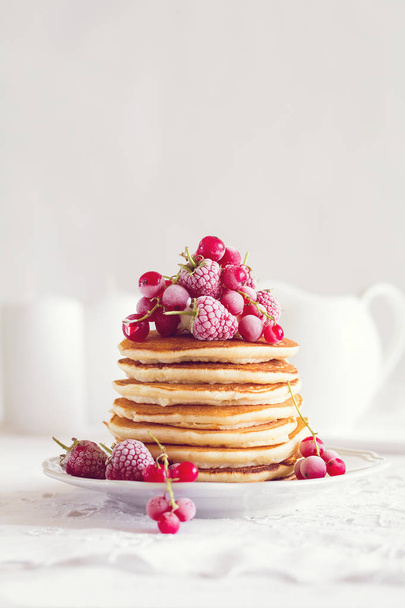 Stack of pancakes with raspberry, red currant, cream and honey on white table cloth - Фото, зображення
