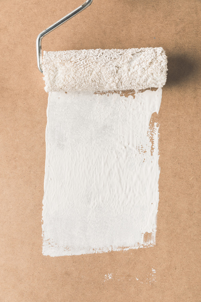 paint roll brush in white paint on plywood surface - Foto, afbeelding