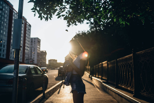 Side view of woman posing on sidewalk at urban city street with sunbeams - Foto, afbeelding