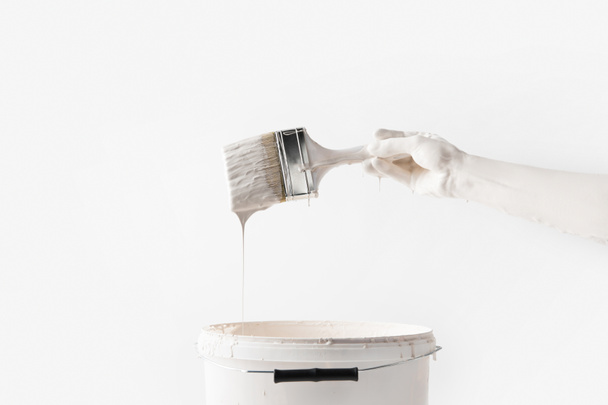 cropped image of woman holding brush in white paint above bucket isolated on white - Foto, immagini