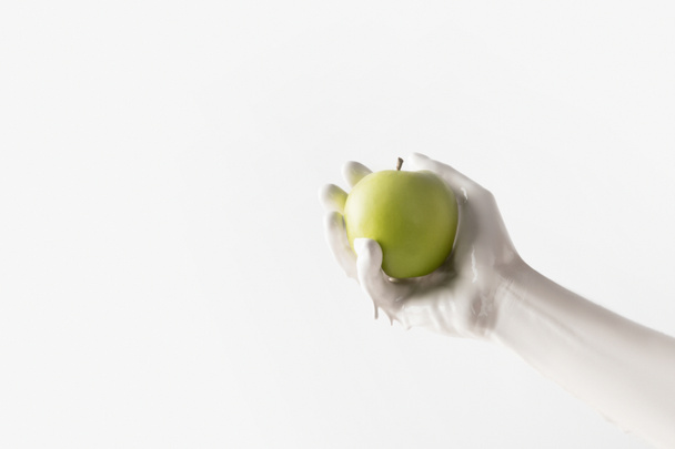 cropped image of woman in white paint holding green apple isolated on white - Fotó, kép