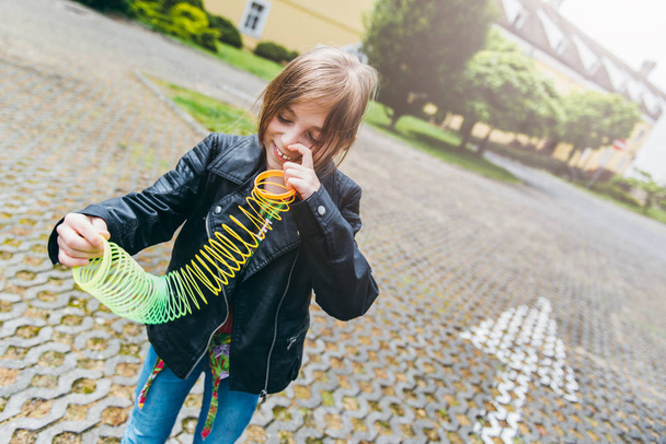 Girl in black leather jacket smiling and playing with colorful spring toy on street - Foto, afbeelding